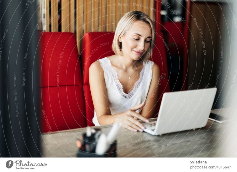 A beautiful blonde girl uses a laptop and works in a cafe. Break, work online, freelance using computer internet business female job businesswoman technology