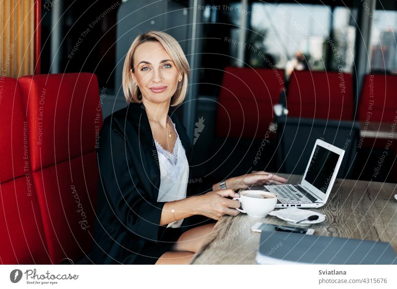 A beautiful blonde girl uses a laptop and works in a cafe. Break, work online, freelance using computer internet business female job businesswoman technology