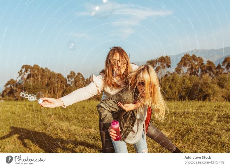 Happy girlfriends riding piggyback and blowing soap bubbles women best friend fun nature together laugh leisure friendship relationship carefree having fun