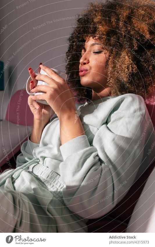 Black woman drinking coffee at home hot beverage enjoy cup afro hairstyle female ethnic african american black sofa tea couch curly hair weekend mug sit
