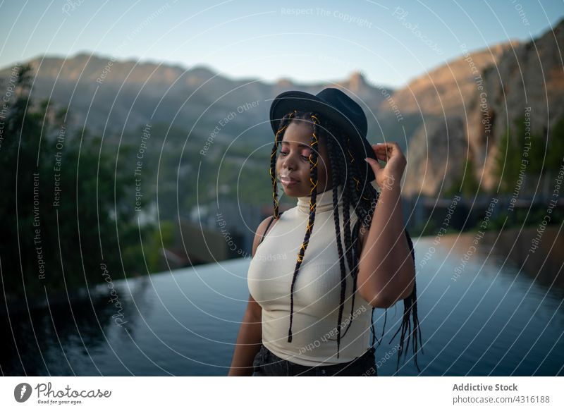 Black woman with braids and hat near swimming pool in mountains resort vacation highland summer hairstyle holiday female black ethnic african american relax