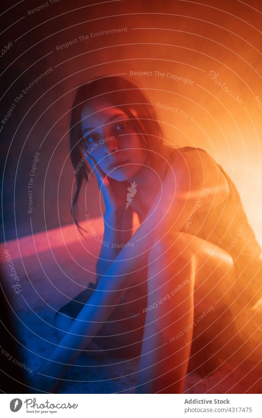 Young woman sitting in neon illumination light dark projector model style art fashion calm alone female young relax confident pensive appearance tranquil
