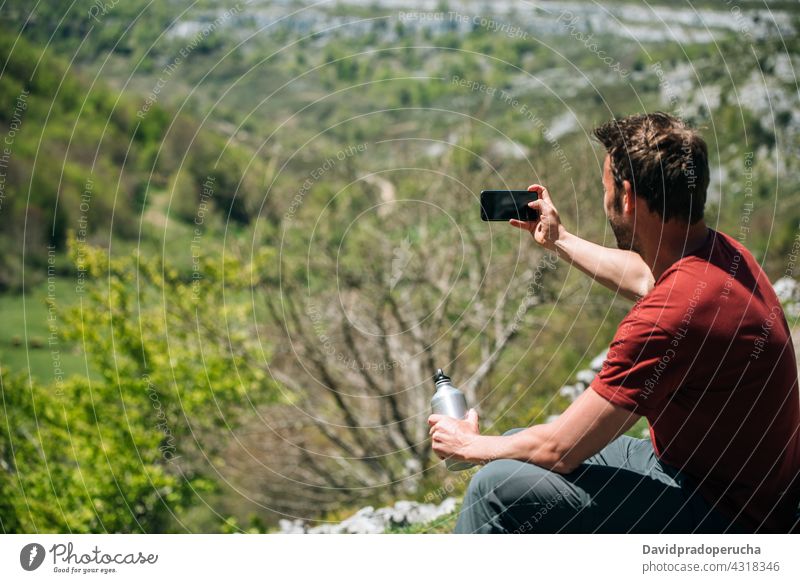 Smiling traveler taking photo with smartphone while resting during hike hiker trekking using positive highland break bottle reuse wanderlust adventure gadget