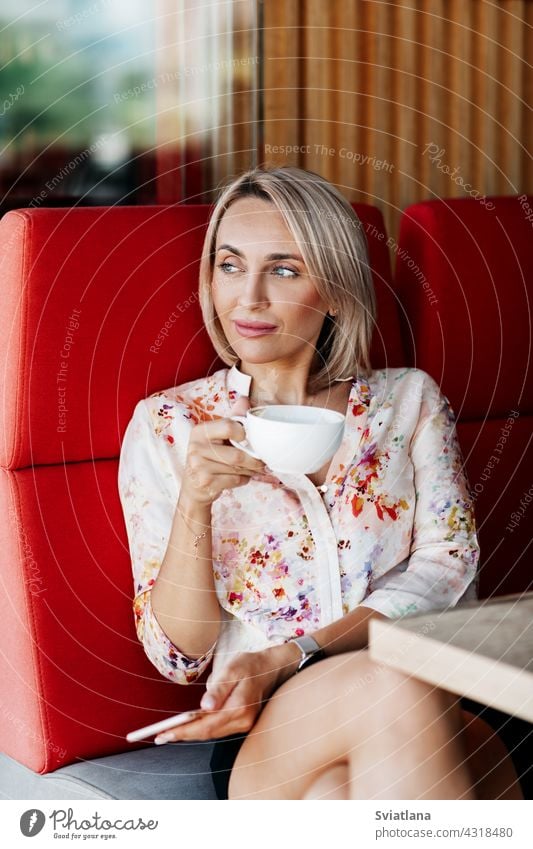 A beautiful girl is drinking coffee in a cafe and looking thoughtfully into the distance woman mobile using message holding people technology business