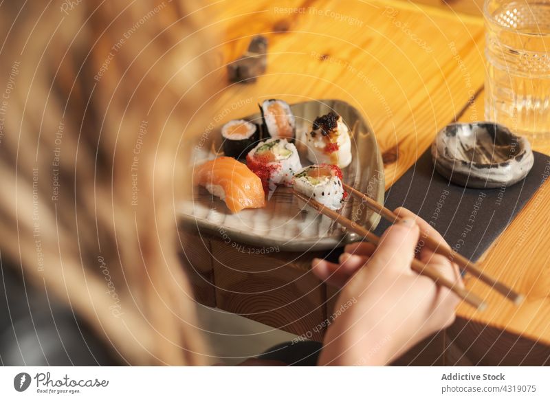 Anonymous woman eating sushi in Asian restaurant roll set asian food asian cuisine delicious tasty female table oriental yummy meal chopstick gourmet fresh