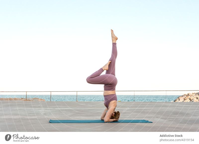Flexible woman doing yoga in Supported Headstand pose headstand balance salamba sirsasana mindfulness zen sea seafront female practice wellbeing wellness mat
