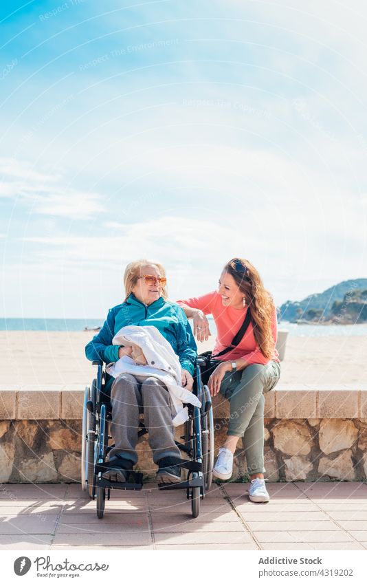 Daughter sitting with aged mother in wheelchair on embankment elderly smile sea disable daughter happy together handicap cheerful promenade seaside seashore