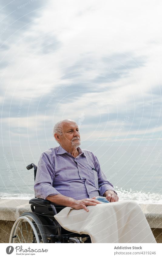 Pensive man in wheelchair on embankment senior sea elderly disable handicap old promenade male retire pensioner aged thoughtful contemplate daytime calm serene