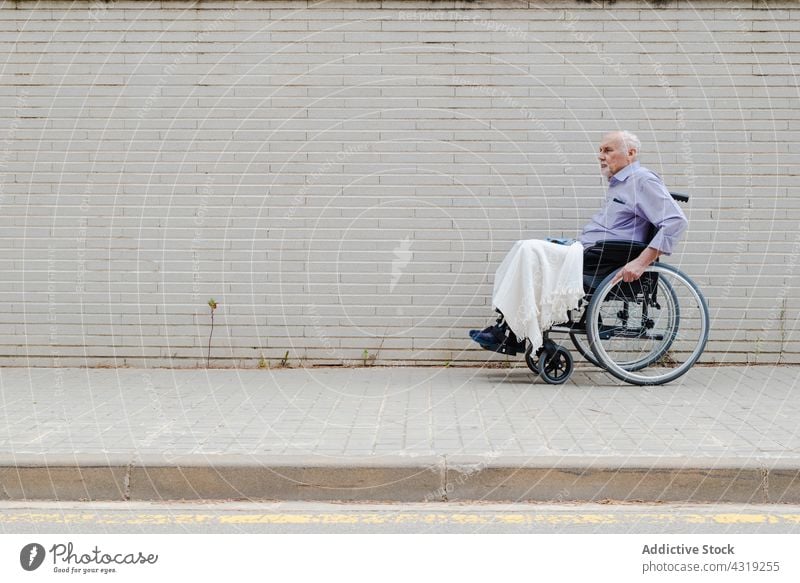 Elderly man in wheelchair riding along street ride city disable aged senior handicap elderly male urban pavement sidewalk town modern move pensioner retire