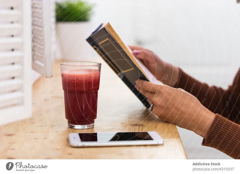 Anonymous African American woman drinking smoothie and reading book in bar refreshment beverage summer chill female black african american ethnic relax rest