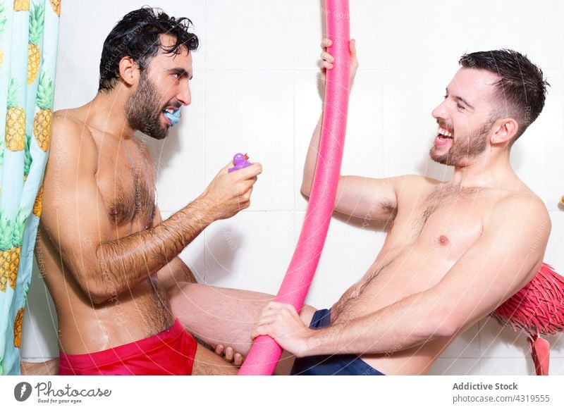 Playful gay couple with toys in bathroom homosexual shower having fun lgbt together men funny play love relationship multiethnic multiracial diverse cheerful