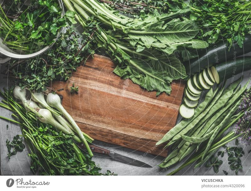 Food background with a frame made with wooden cutting board and various green vegetables and herbs for tasty and healthy cooking. Top view. food background