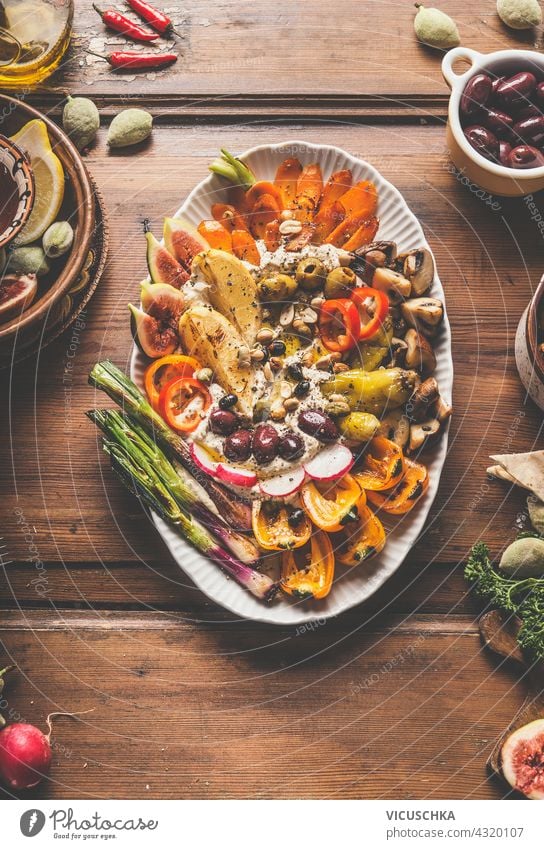 Plate with freshly homemade hummus, grilled vegetables and a variety of nuts and seeds toppings. Healthy vegan food. Lunch or snack on rustic wooden background. Top view