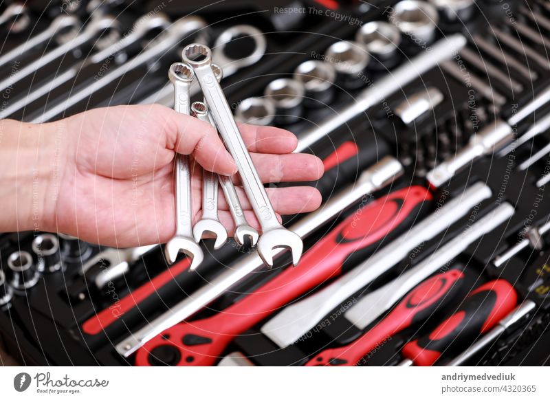 Tool store. Closeup of male hand holding wrenches. Auto repair kit in toolbox. Repairman instruments set. Inside the toolbox there are black-red wrenches, spanners and different nozzles. Closeup.