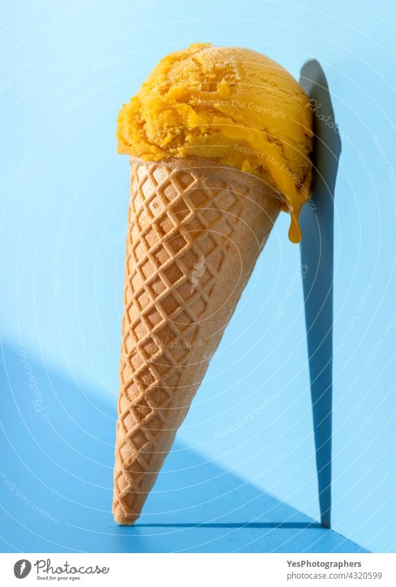 Mango ice cream in bright light, on a blue background. ball close-up cold color concept cone copy space cut out delicious dessert drip flavor food frost frozen