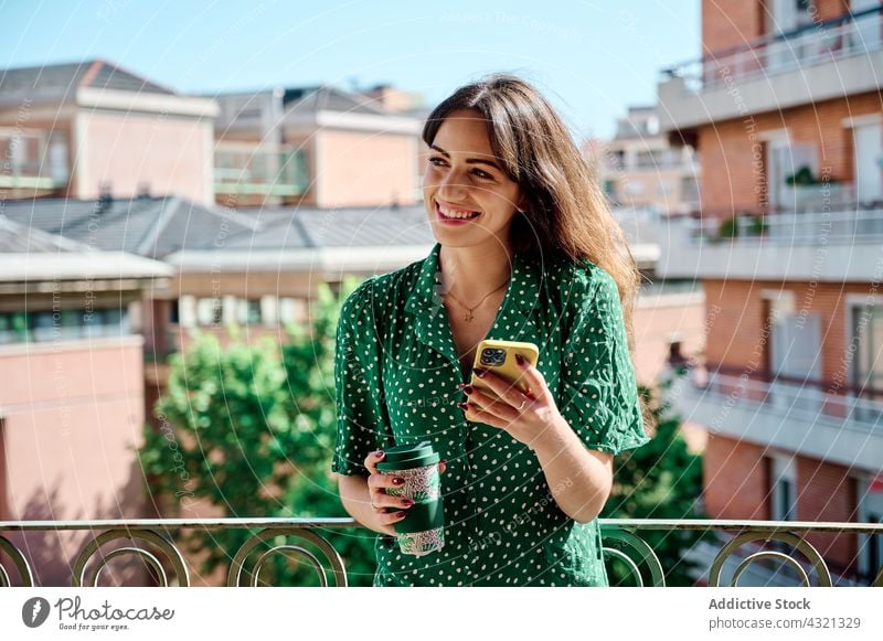 Smiling woman drinking coffee and using smartphone on balcony mobile beverage summer female browsing social media terrace internet content smile gadget device