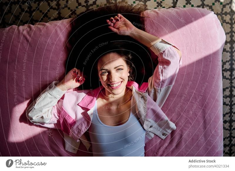 Carefree woman lying on bed at home comfort relax sunlight shadow bedroom cozy soft female rest enjoy shade charming calm harmony cheerful chill weekend smile