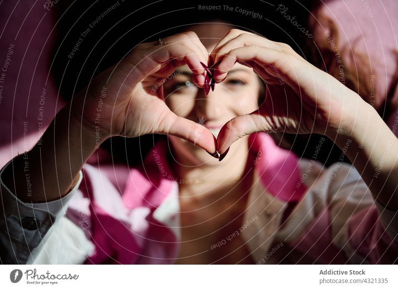 Woman showing heart gesture at camera woman love sign valentine cheerful romantic shape symbol female smile happy positive style content enjoy optimist creative