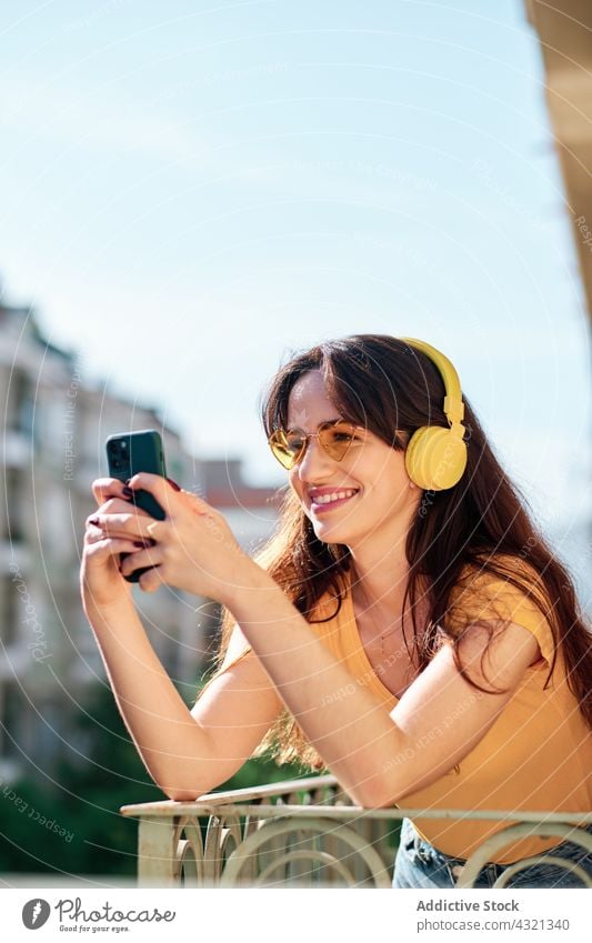 Happy woman in headphones listening to music on balcony smartphone using enjoy song melody female gadget device mobile summer browsing relax positive playlist