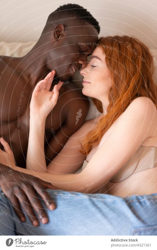 Gentle multiracial couple relaxing on bed at home tender love together smile kiss stroke caress relationship gentle multiethnic diverse black african american