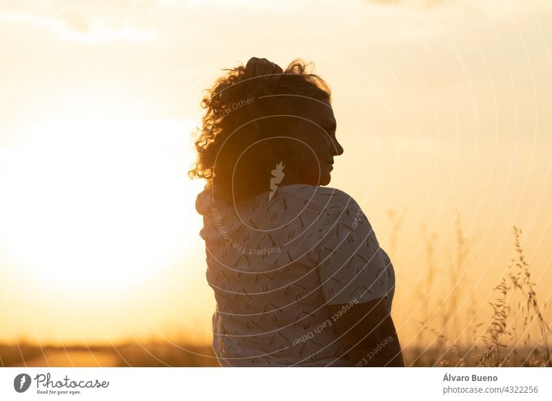 An adult woman enjoys the sun and adjusts her gray hair with her hand during a walk in the field at sunset, Spain elderly woman walking enjoying the field