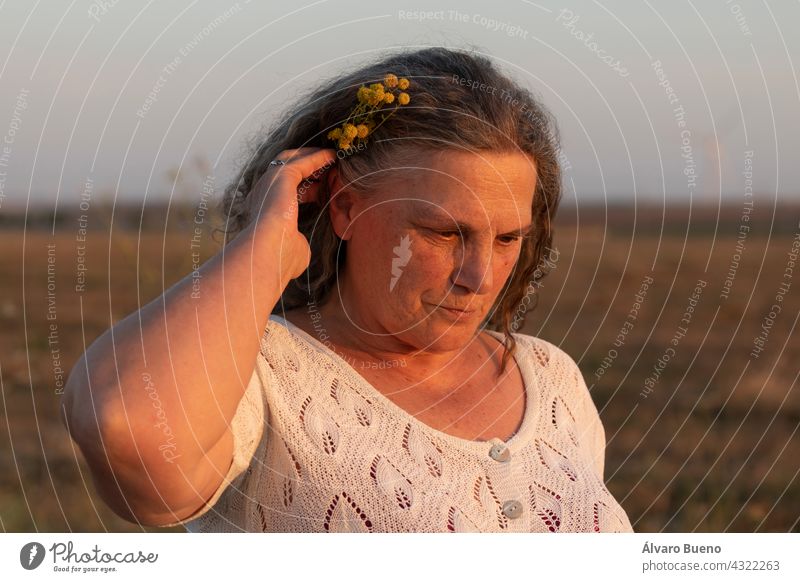 An adult woman adorns her hair with a small bouquet of yellow chamomile flowers while taking a walk in the countryside, Spain elderly woman walking