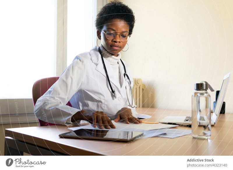 Black female doctor working with papers in office clinic medic read health care practitioner woman document young african american black ethnic professional job