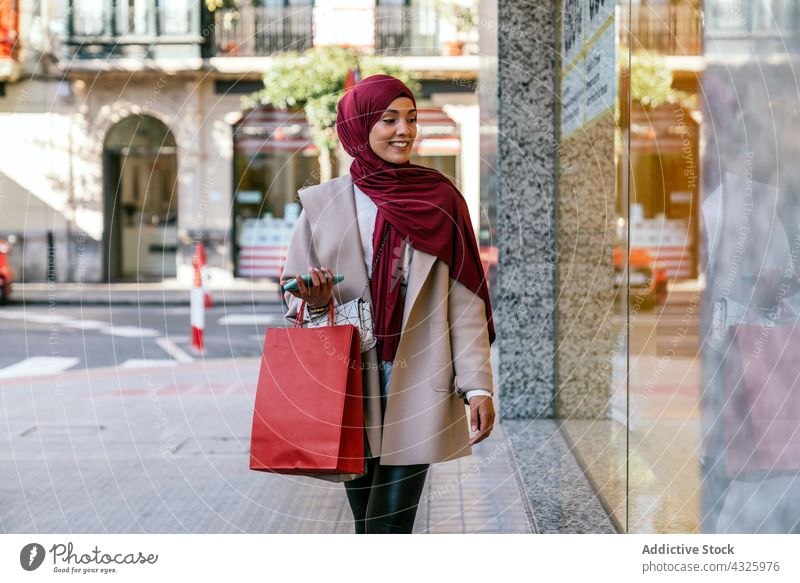 Smiling Muslim woman with shopping bags near showcase shopper city store buyer shopaholic customer female ethnic muslim sale consume mall choose consumerism
