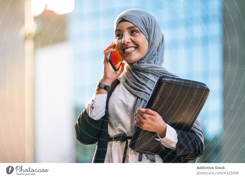 Muslim businesswoman talking on smartphone in city entrepreneur hijab discuss conversation mobile speak female ethnic muslim gadget work smile headscarf