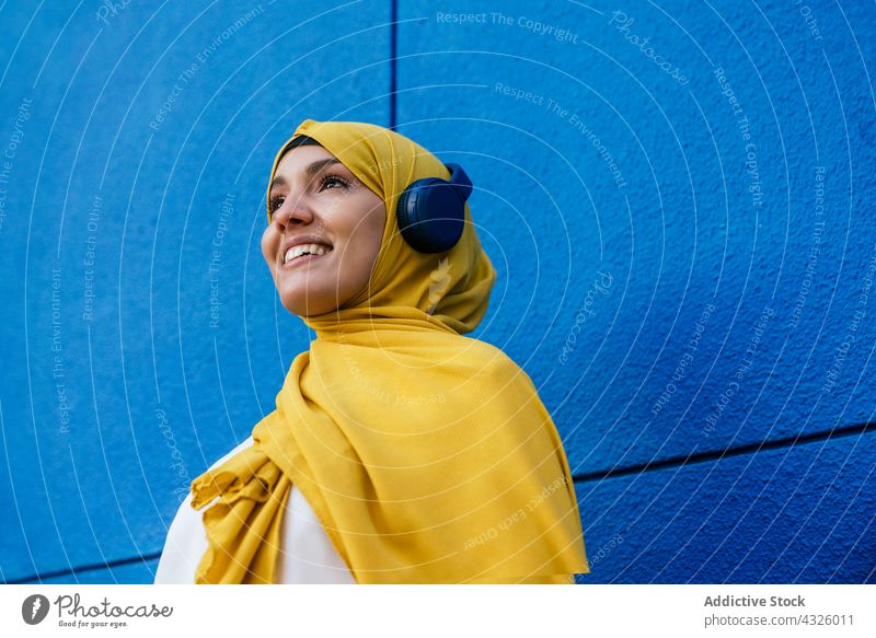 Happy muslim woman listening to music in headphones hijab city female ethnic device gadget headscarf song style sound urban yellow headdress headwear tradition