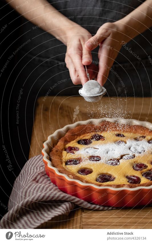Crop cook adding powdered sugar on cherry clafoutis pie delicious homemade person apron baked wooden table dessert pastry food tasty cake sweet bakery gourmet