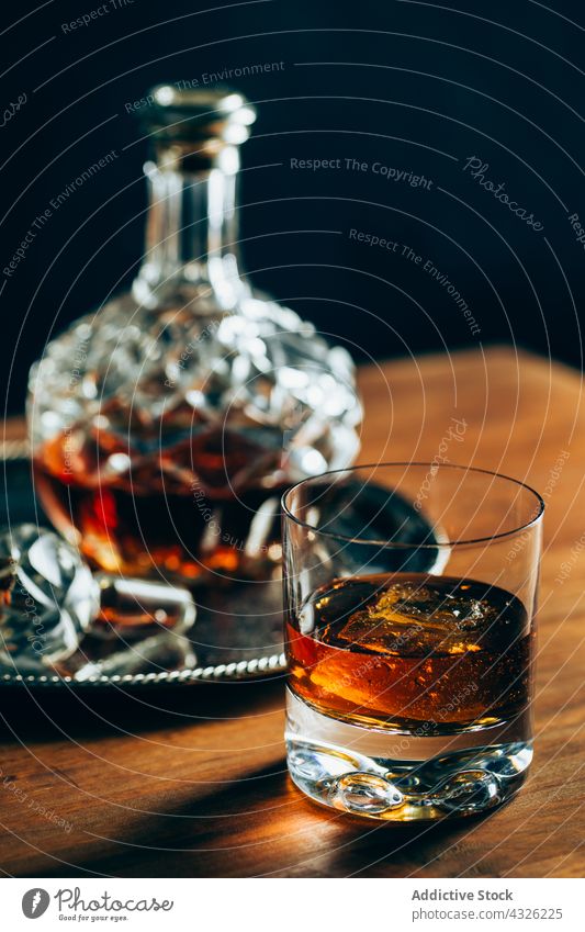 Glass of whiskey near decanter glass table cup cold ice drink alcohol dark crystal bottle container beverage liquid cool composition booze lumber timber wooden