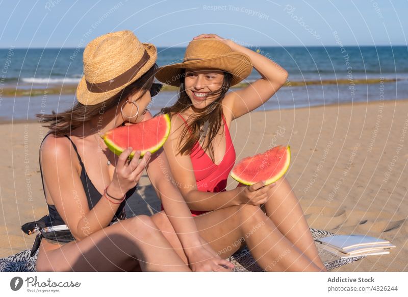 Cheerful woman eating watermelon on seashore friend beach women summer swimsuit vacation together seaside female sand fruit happy cheerful girlfriend enjoy