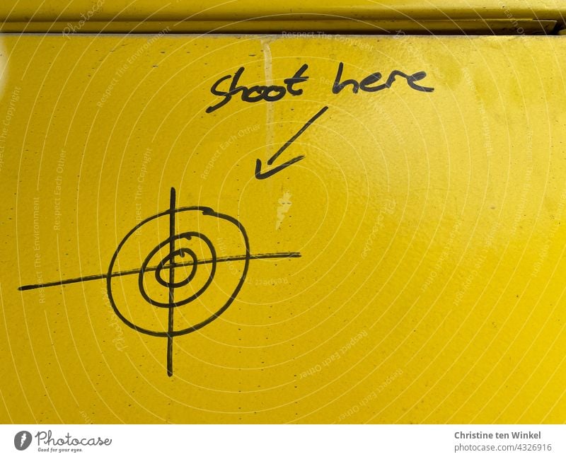 painted shooting target and the text "shoot here" and an arrow on bright yellow metal | drawn & painted Graffito Arrow Text Metal Yellow Wall (building) Daub