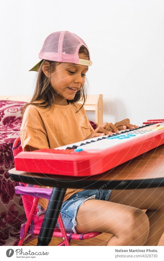 Little hispanic girl wearing a pink cup playing in a red piano in her bedroom pianist person chord classical finger rythm create practicing performance melody