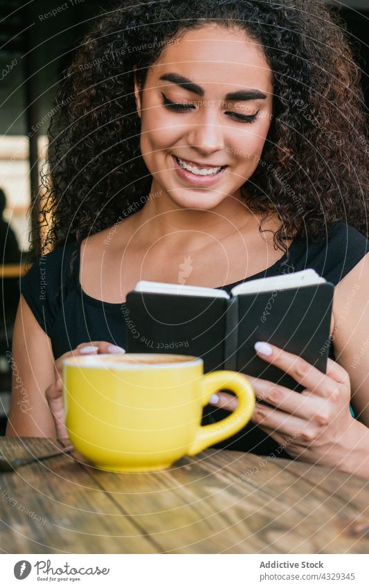 Happy woman reading notebook in cafe coffee smile happy cup enjoy coffee break female young ethnic hispanic curly hair terrace rest drink cheerful positive