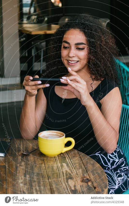 Ethnic woman using smartphone in outdoor cafe coffee take photo cup happy free time female young hispanic ethnic curly hair enjoy terrace drink cheerful
