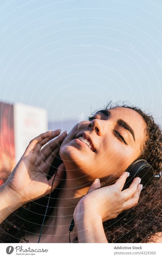 Young woman in headphones enjoying music on street listen chill relax carefree happy song female young ethnic hispanic curly hair summer positive lifestyle