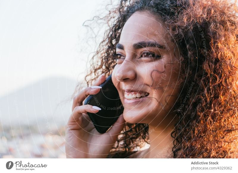Happy Hispanic woman speaking on smartphone talk happy smile curly hair communicate cheerful conversation female young ethnic hispanic human face mobile enjoy