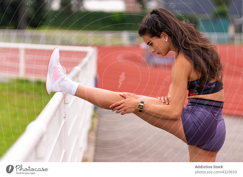 Sportswoman stretching legs on stadium sportswoman athlete runner warm up track workout training young hispanic ethnic exercise activity lifestyle female