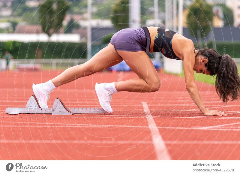 Female athlete ready to sprint on stadium track sportswoman sprinter crouch start block runner female young hispanic track and field workout determine