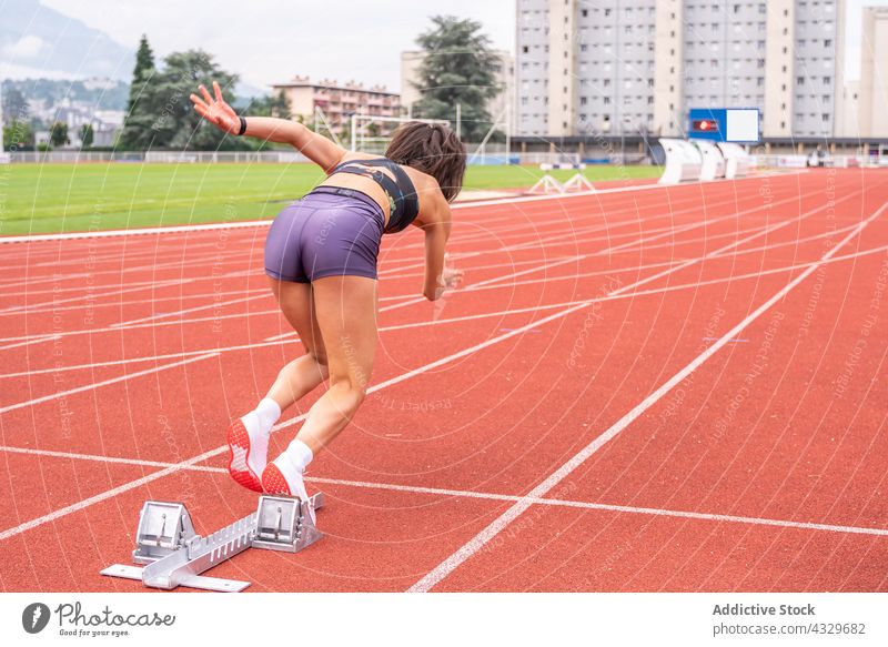 Athletic woman starting sprint at stadium sportswoman athlete sprinter track runner determine race fast speed motion block action female young hispanic