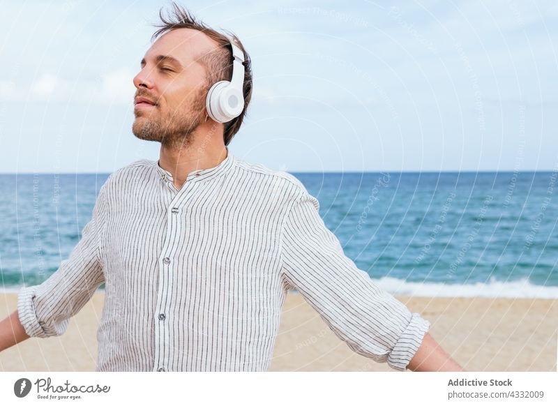 Relaxed man in headphones enjoying summer day on beach relax happy listen music sea carefree male young beard wireless lifestyle gadget device guy trendy rest