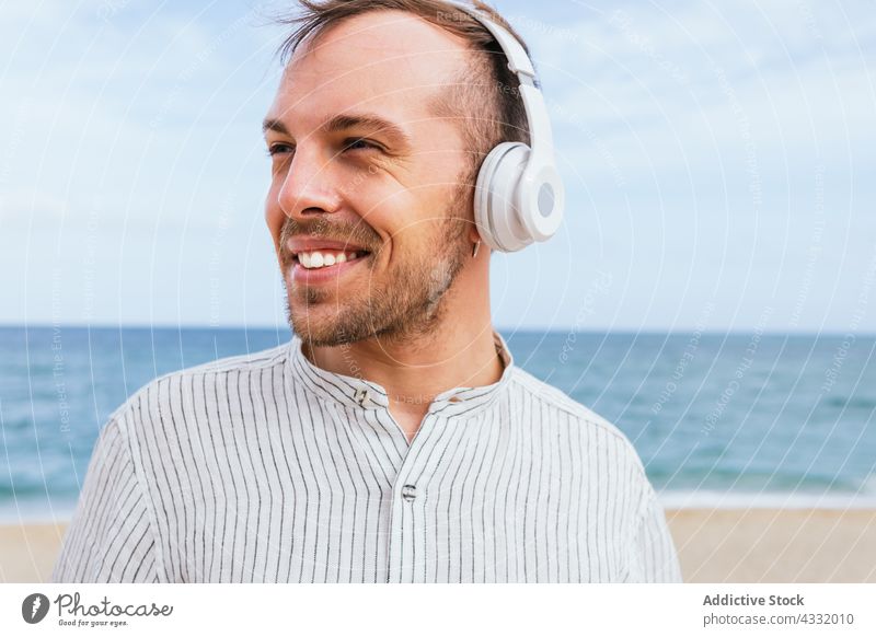 Happy relaxed man in headphones enjoying summer day on beach happy listen music sea carefree male young smile beard wireless lifestyle gadget device guy trendy