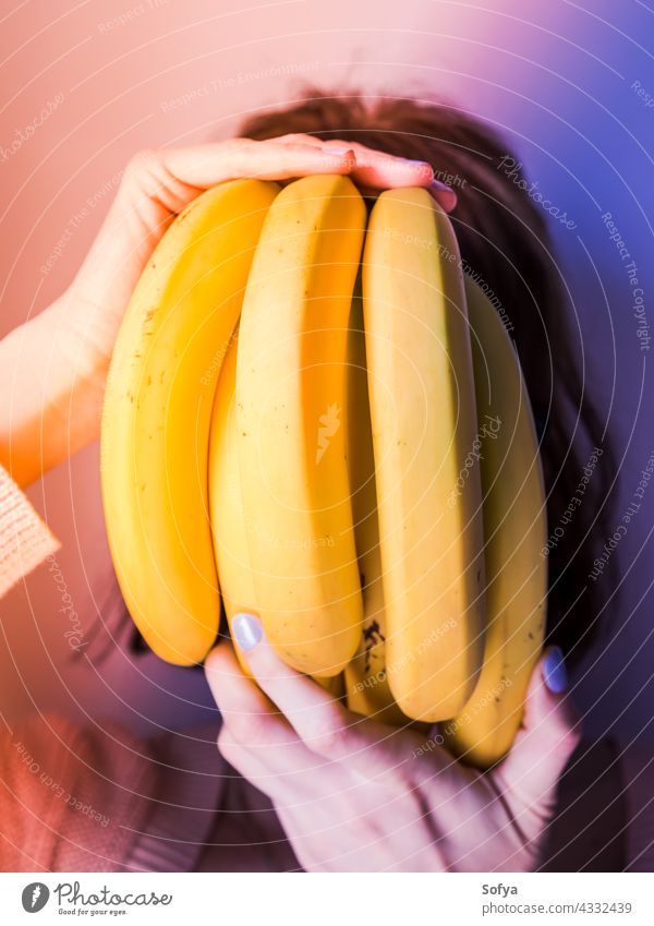 Woman covering face with bunch of bananas. Neon art woman purple hand manicure neon food design concept modern trends diet fashion gradient female color light