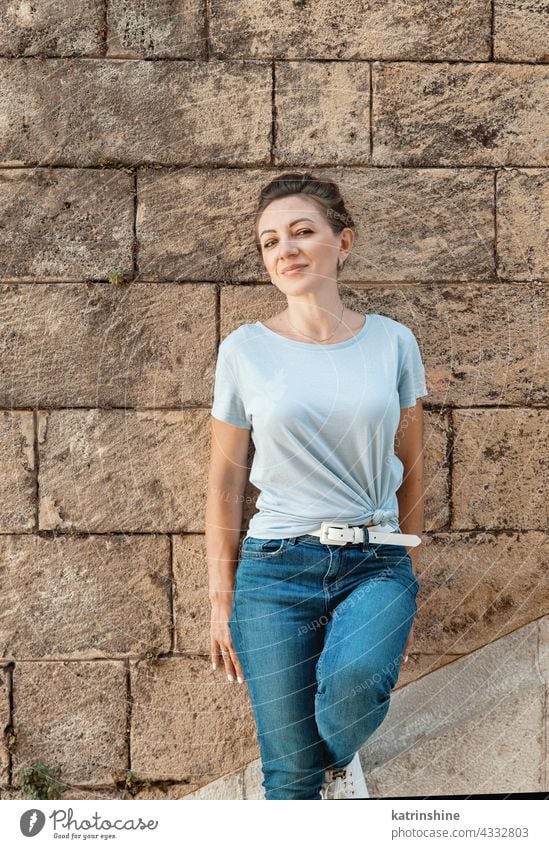 Women wearing t-shirt and jeans stays near a wall adult Middle aged women smile casual mock up Outdoor fair haired millennials copy space Person Portrait lady