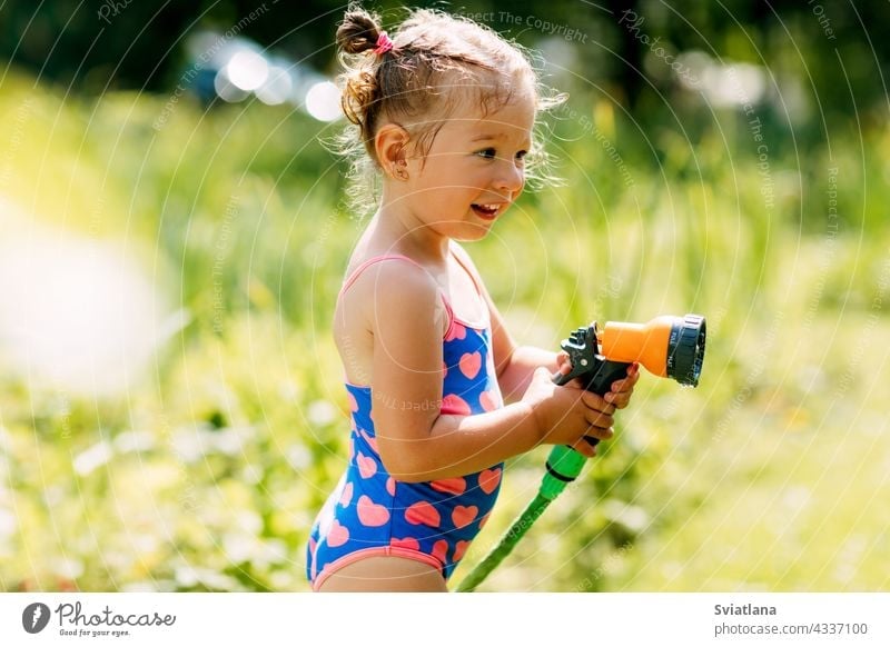 Charming baby girl waters plants with a hose in the garden in the backyard of the house on a sunny summer day child little spray childhood toddler beautiful