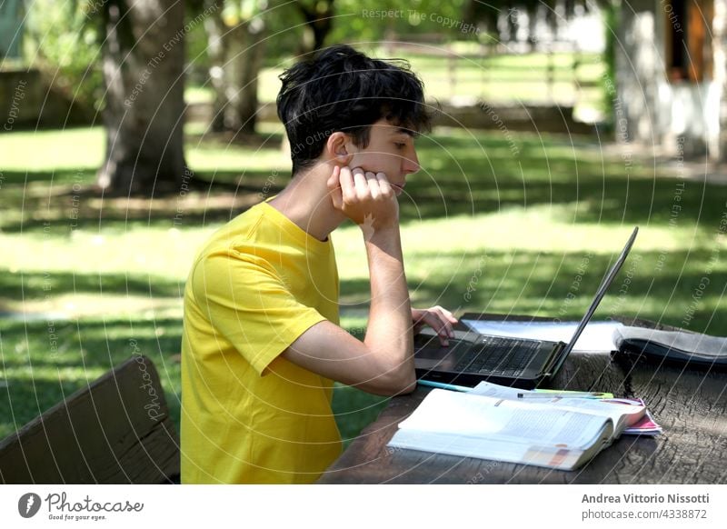 male teenager studying outside in a garden with copy space for your text boy student personal computer technology book textbook copybook equipment table sitting