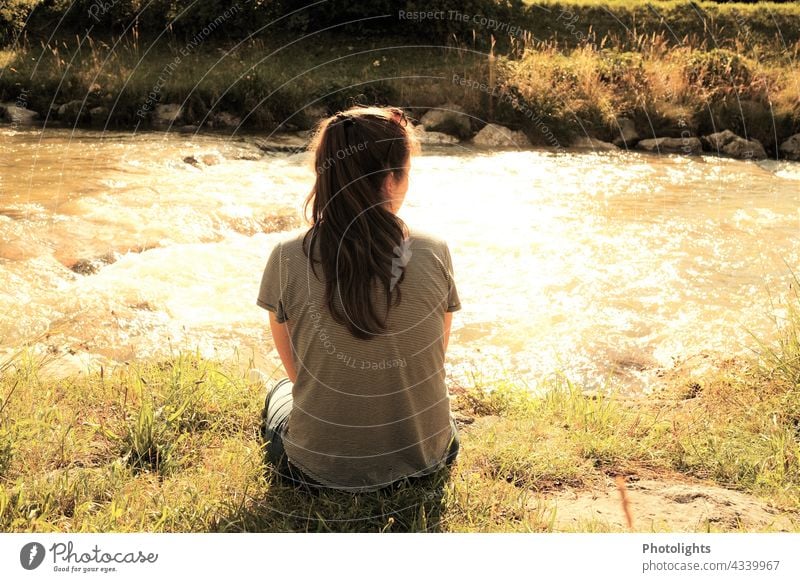 Young woman sitting by a stream in the evening sun. shore zone Water River Long-haired Life Serene Dream Beautiful weather Light Exterior shot Colour photo