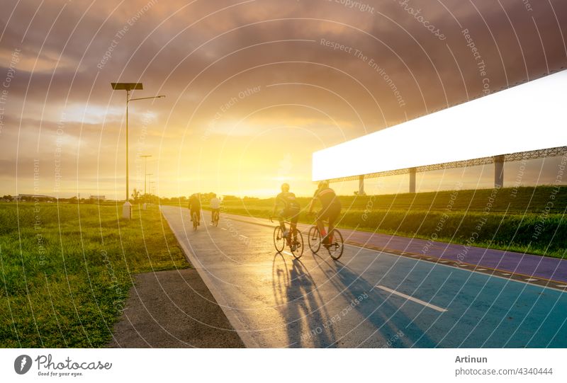 Sports man ride bicycles on the road in the evening near blank advertising billboard with sunset sky. Summer outdoor exercise for healthy and happy life. Cyclist riding mountain bike on bike lane.